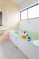 Un baño con bañera, ducha y varios artículos de aseo sobre el borde.