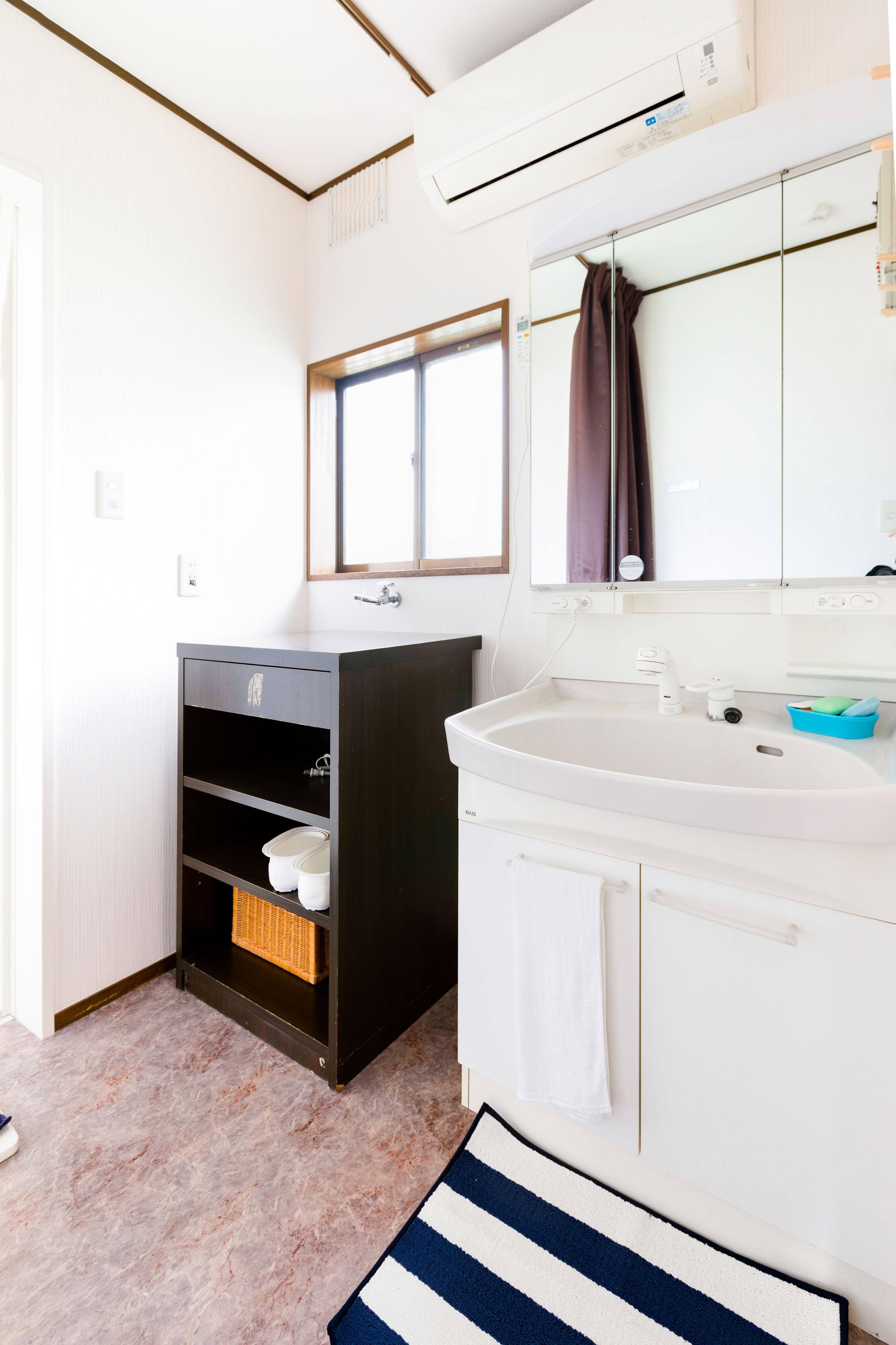 A bathroom with a white sink, a mirror, a window, and a black cabinet with shelves.