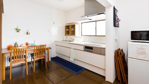 A compact kitchen with a dining area, white cabinets, a microwave, and a small refrigerator. - A&Z guesthouse (Kaizuka)