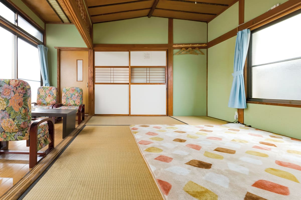 A traditional Japanese room with tatami flooring, a shoji screen door, and floral-patterned furniture.