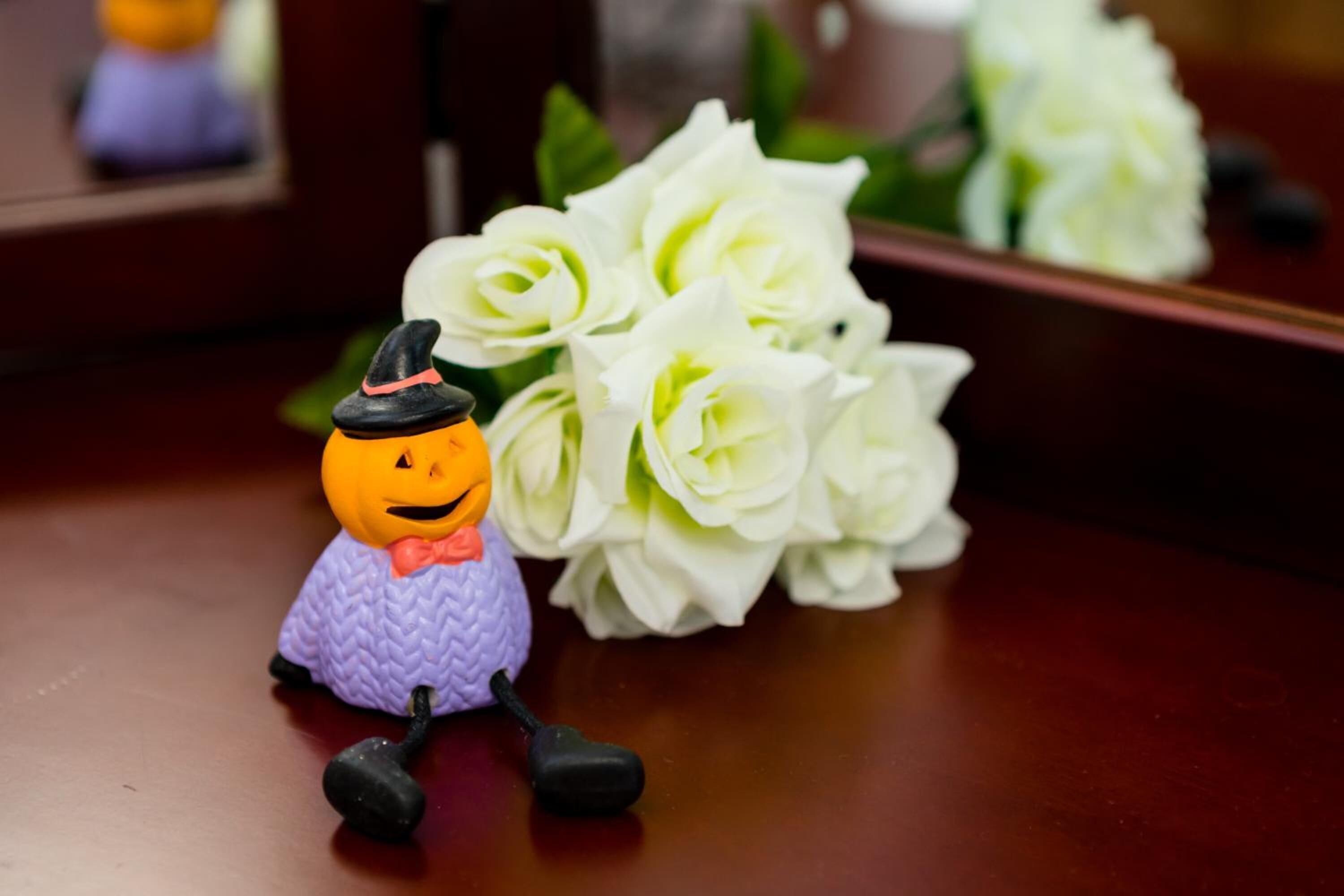 A small pumpkin figurine with a witch hat and bow tie on a table next to a bouquet of white flowers.