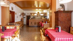 A restaurant with wooden tables and chairs, a bar area, and a decorative cabinet. - Hotel Stella Alpina (Predazzo)