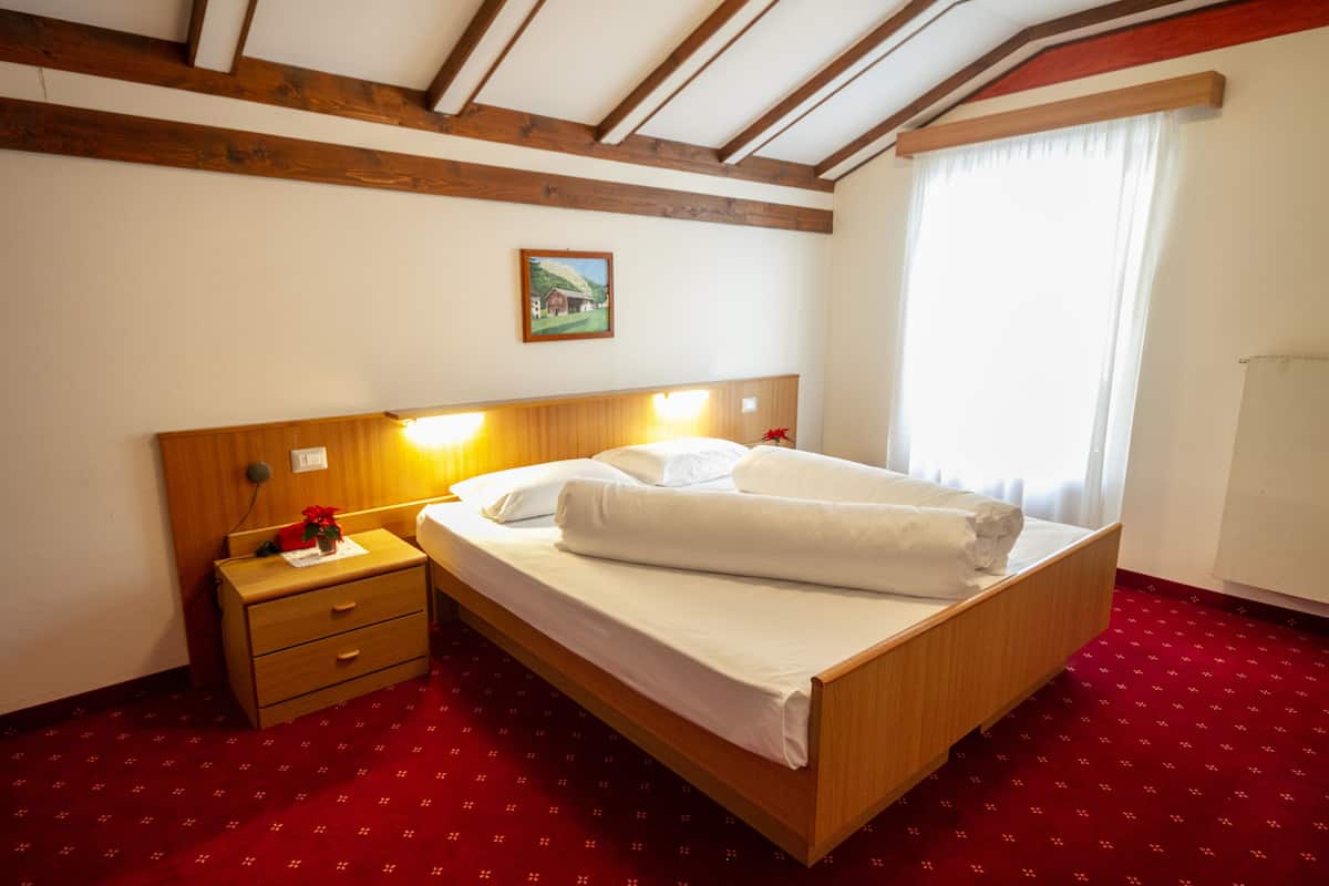 A hotel room with a wooden bed, a nightstand, a red carpet, and a painting on the wall.