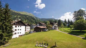 A rural village with traditional wooden houses, a grassy field, and mountains in the background. - Hotel Stella Alpina (Predazzo)