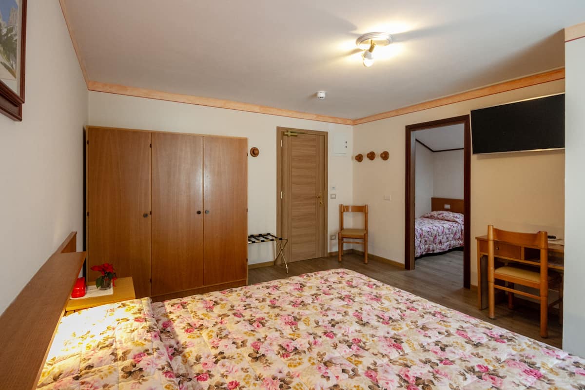A bedroom with a bed, a wooden wardrobe, a desk, and a chair.