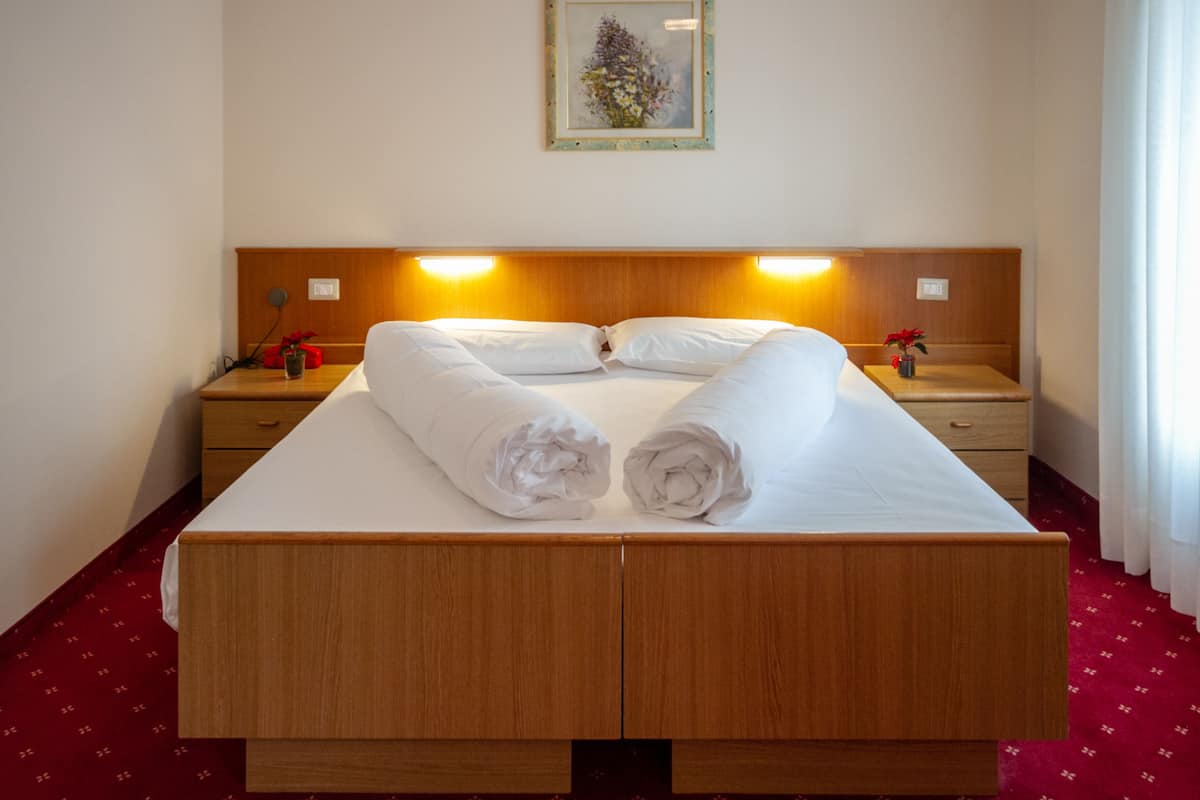 A hotel room with a wooden bed, two bedside tables, a nightstand, and a framed picture on the wall.