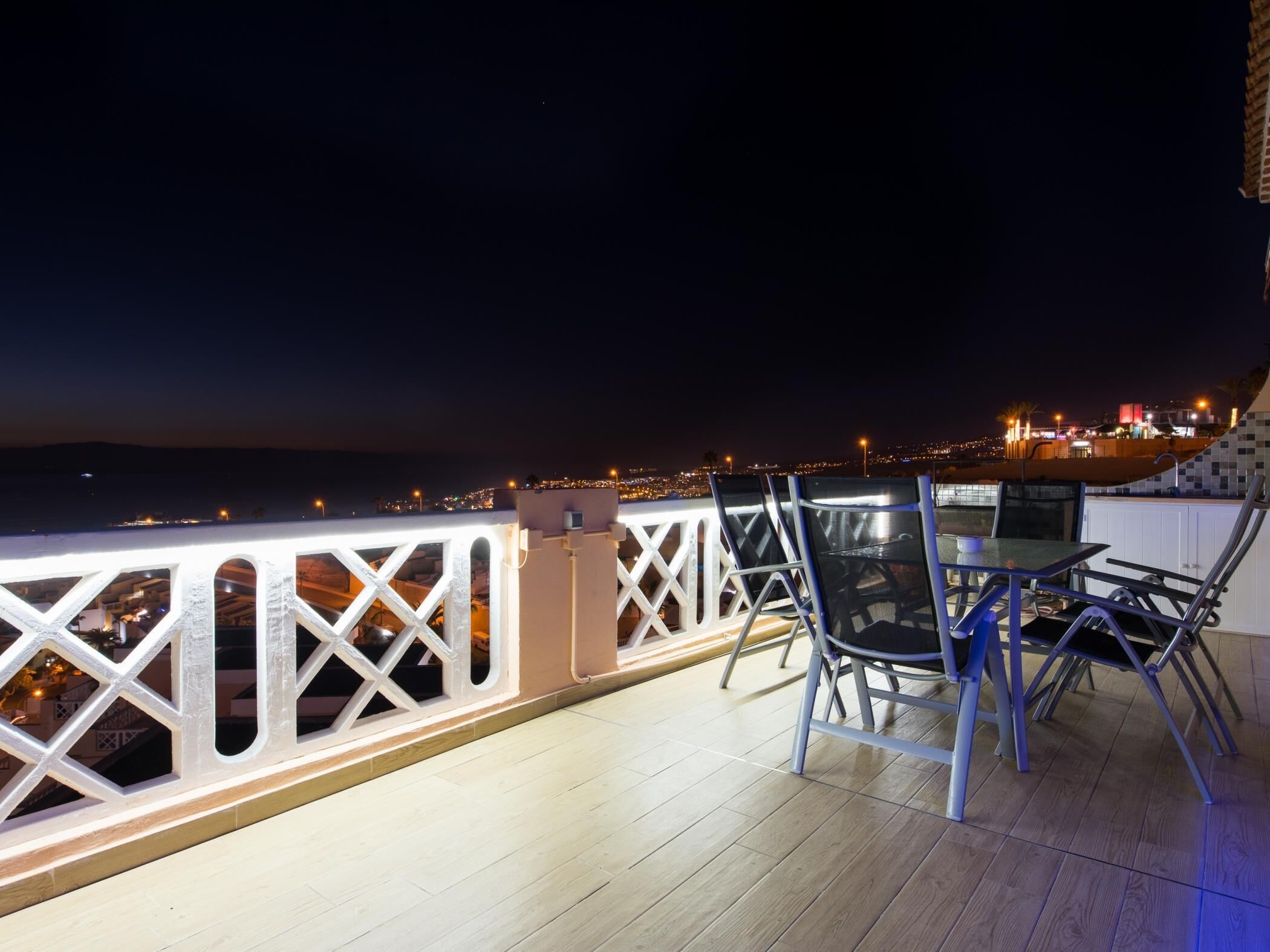 Un balcón con vista a la ciudad de noche, que incluye una mesa y sillas.