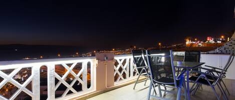 Un balcón con vista a la ciudad de noche, que incluye una mesa y sillas.