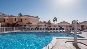Uma piscina com espreguiçadeiras e um edifício com telhado telhado ao fundo.