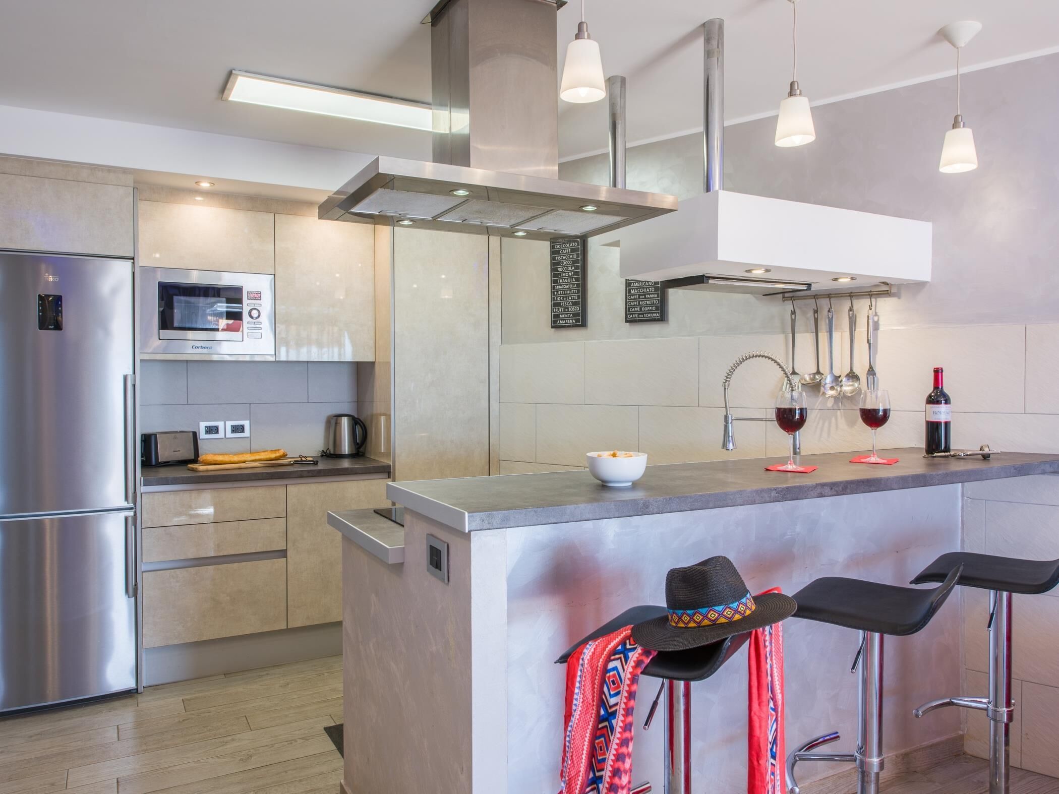 Una cocina moderna con electrodomésticos de acero inoxidable, una isla central, lámparas colgantes y una barra con taburetes.