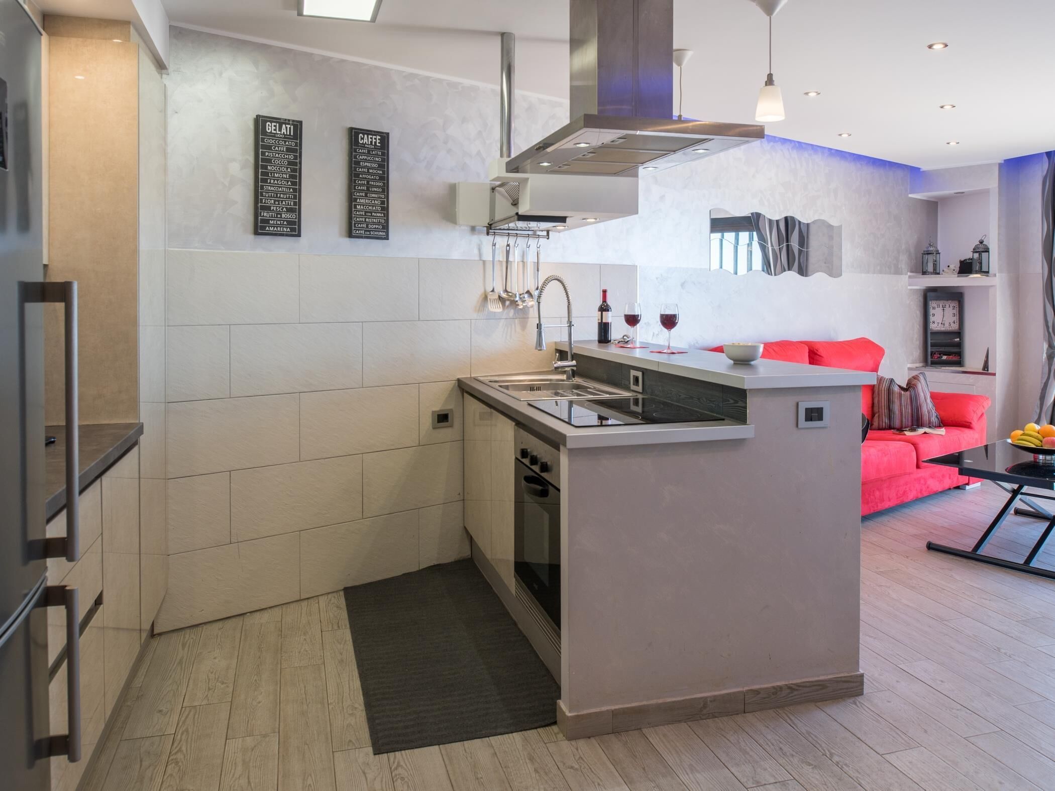 A modern kitchen with a built-in island, a dining area with a red sofa, and a living room with a TV.