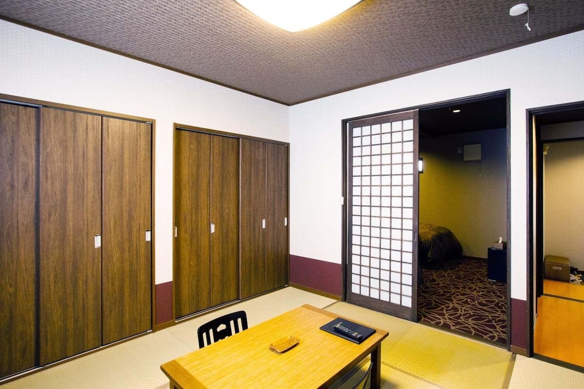 A hotel room with a wooden table, chairs, a bed, and a sliding door.