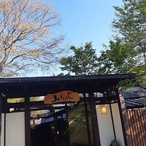 A traditional Japanese gate with a wooden sign, surrounded by trees and a clear sky. - Yamamomiji (Yufu)