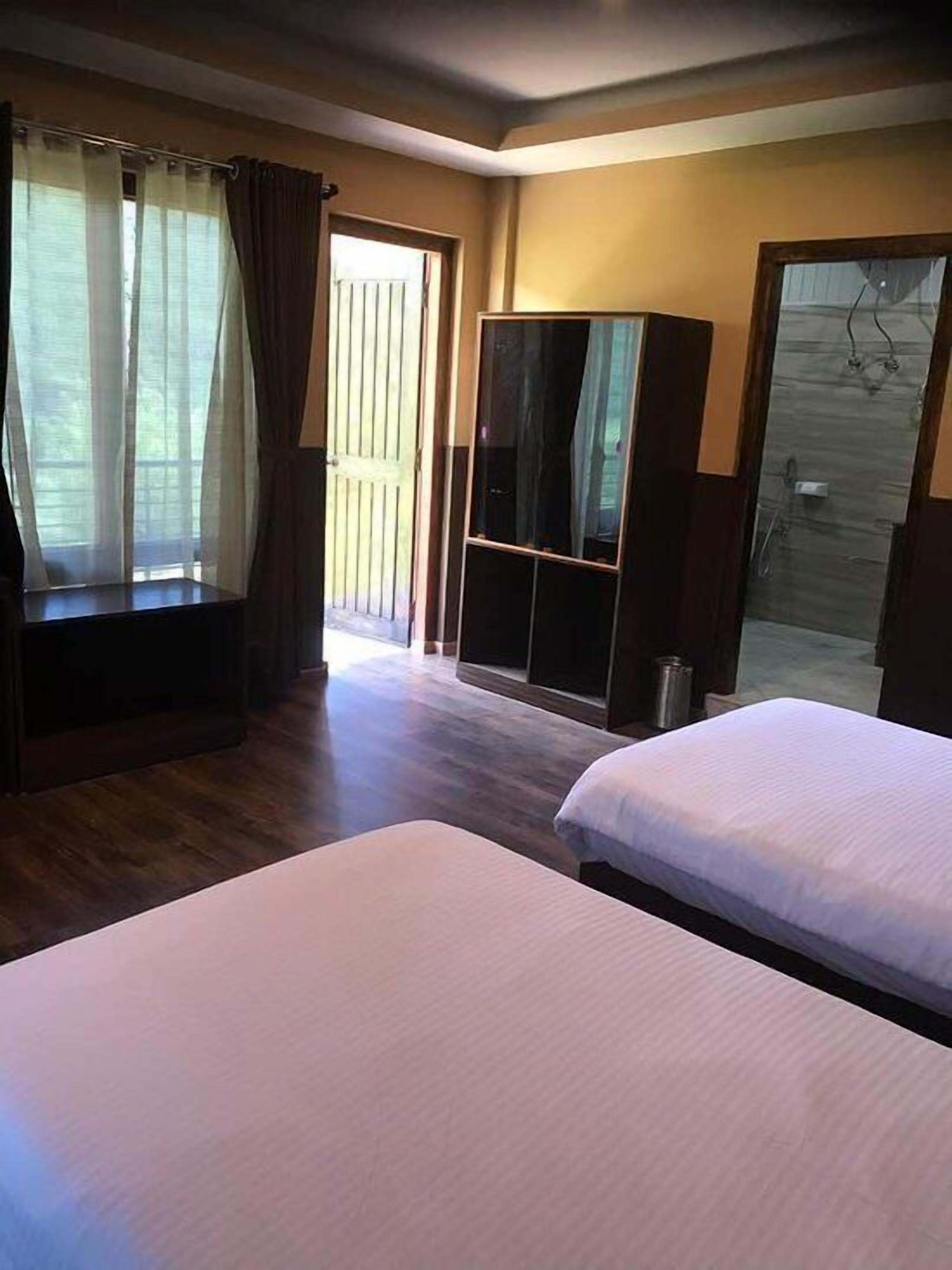 A hotel room with two beds, a large mirror, a wardrobe, and a sliding glass door leading to a balcony.