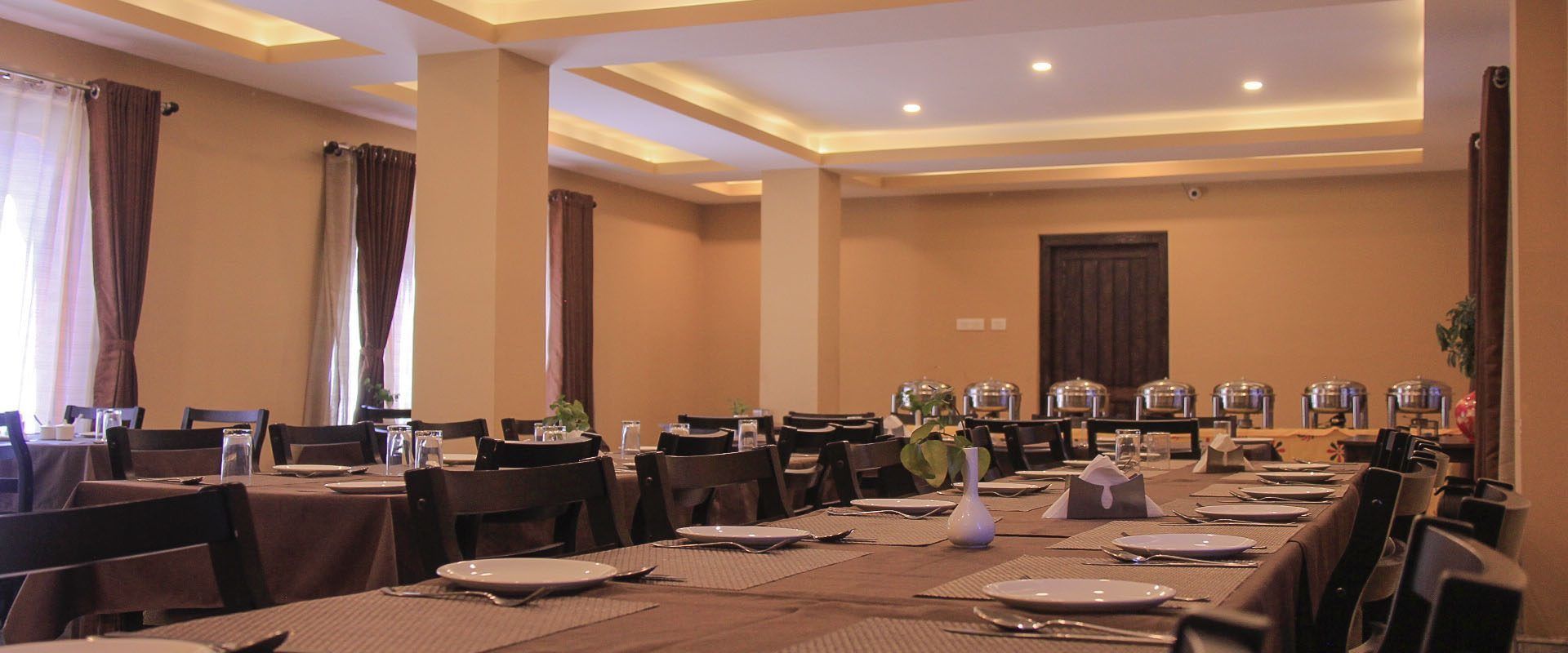 A hotel dining room with tables set for meals, chairs, and a large window with curtains.