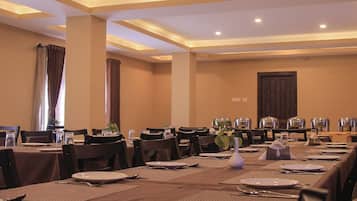 A hotel dining room with tables set for meals, chairs, and a large window with curtains.
