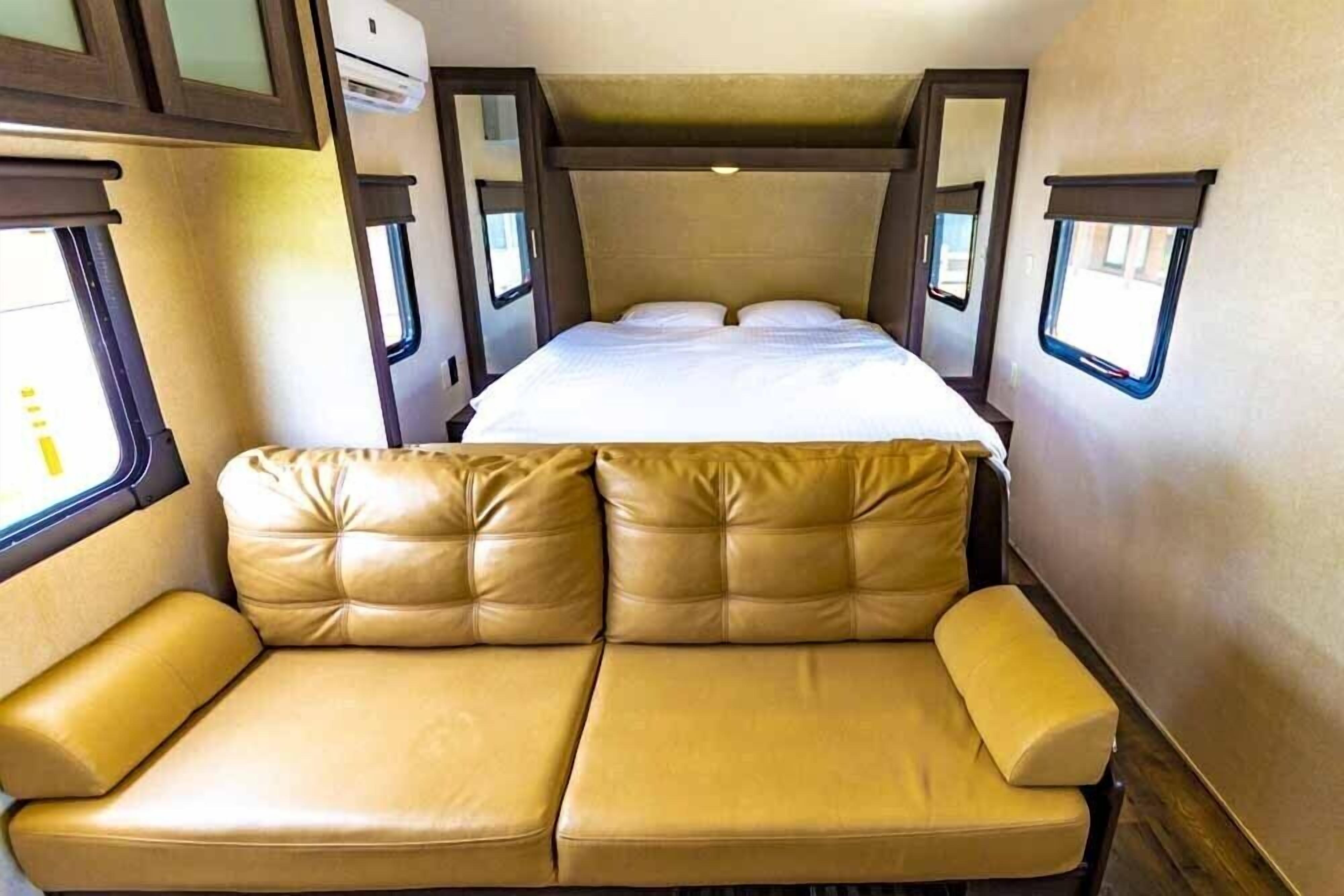 Interior compacto de una autocaravana con cama, sofá y una ventana pequeña.