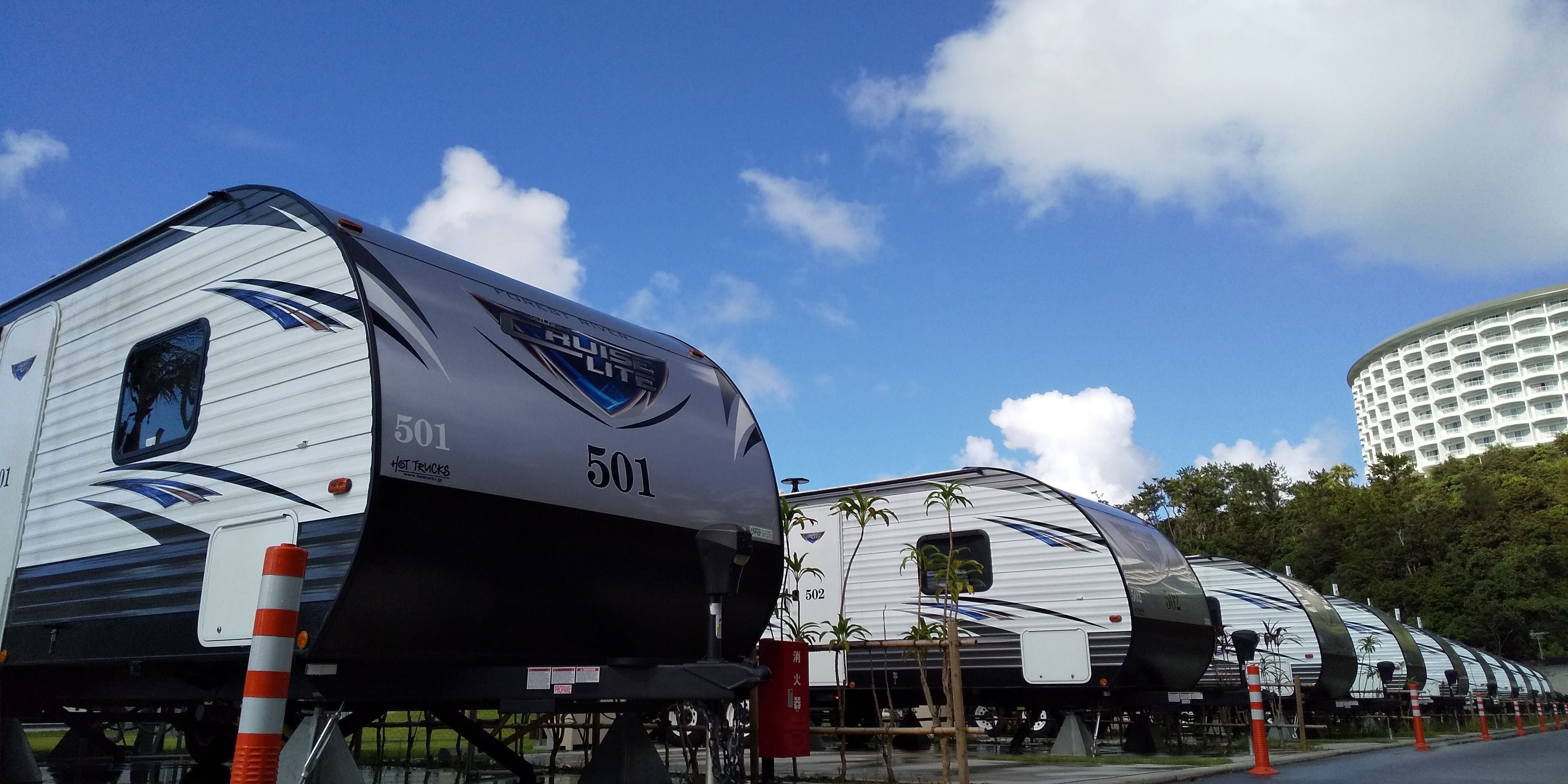 Una hilera de autocaravanas con el número 501, estacionadas al aire libre bajo un cielo despejado y un edificio moderno al fondo.