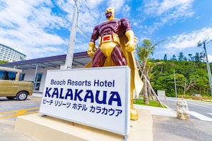 A sign for Beach Resorts Hotel Kalakaua with a large statue of a superhero in the background. - Beach Resorts Hotel KALAKAUA (Onna)