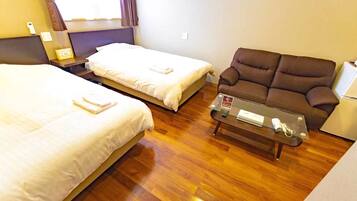 Habitación de hotel con dos camas individuales, un sofá marrón, una mesita con un control remoto y una ventana con cortinas.