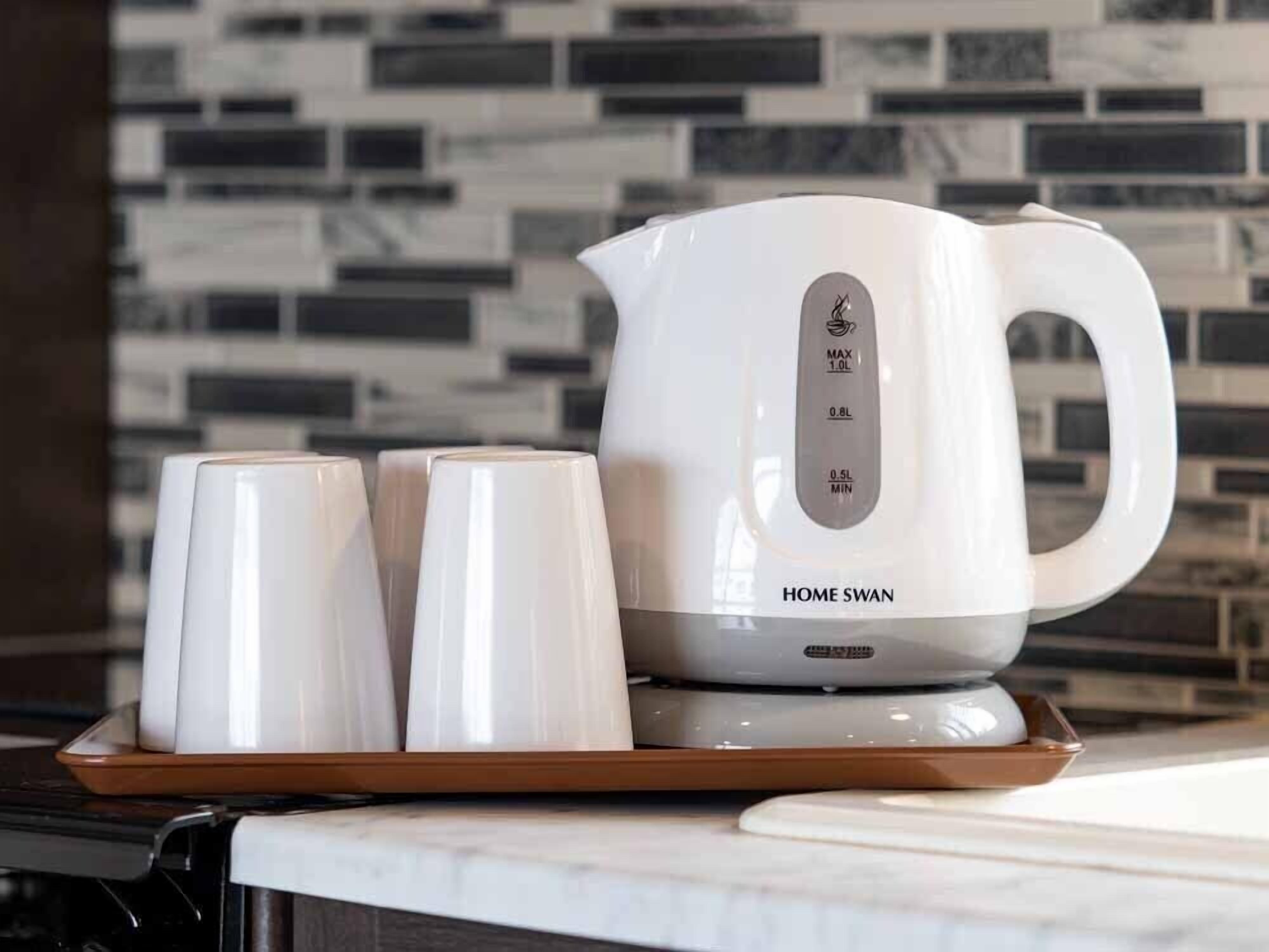 A white electric kettle with measurement markings and the brand name "HOME SWAN" on a tray with two white cups.