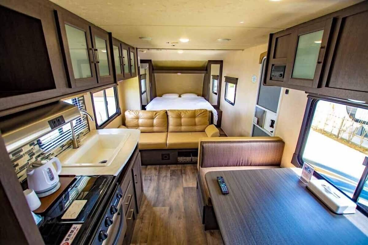Interior de una caravana compacta con cocina americana, una cama con cabecera y una zona de estar.