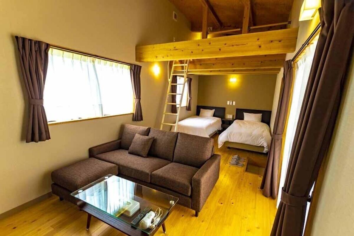 Una habitación acogedora con un sofá, una mesa de centro de vidrio, una cama litera y una escalera.