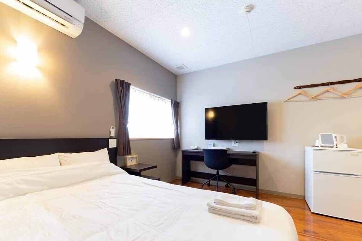 Habitación de hotel con una cama grande, un escritorio con silla, televisor de pantalla plana y un refrigerador pequeño.