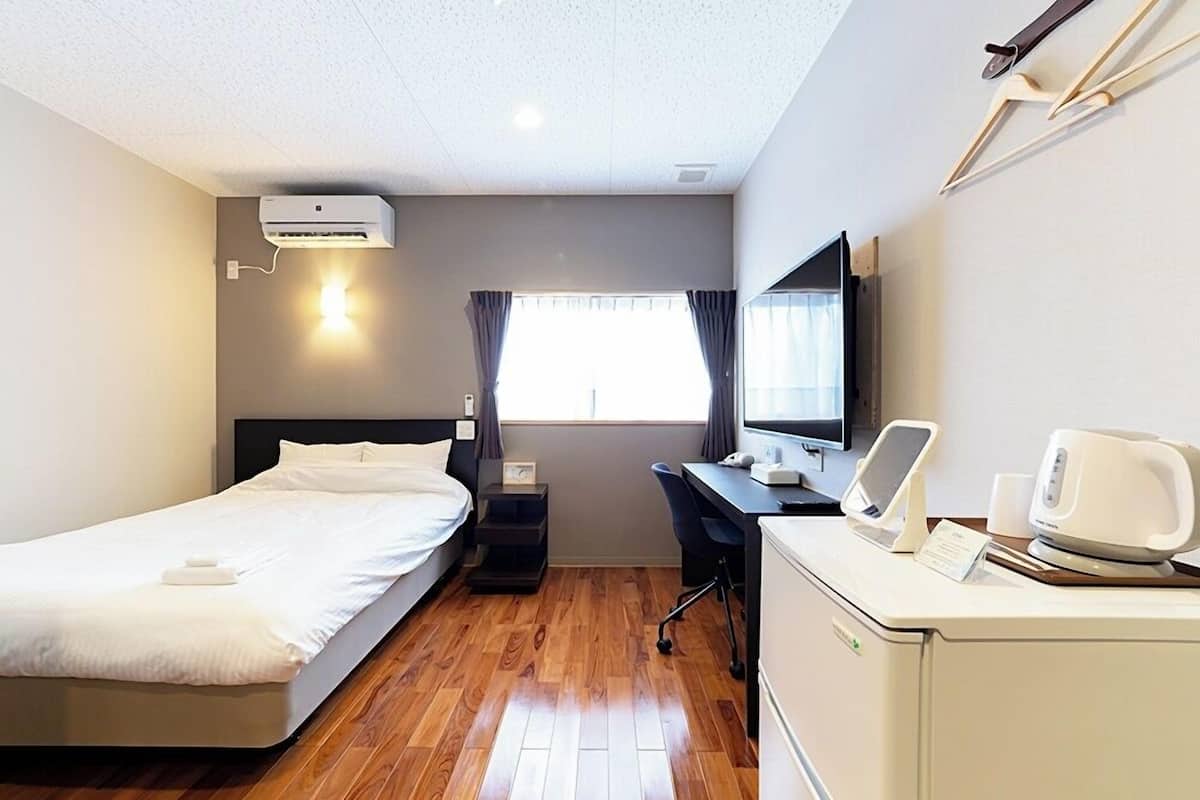 Habitación de hotel con cama, escritorio, computadora y una kitchenette pequeña.
