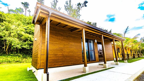 A modern wooden building with a covered porch, surrounded by lush greenery. - Beach Resorts Hotel KALAKAUA (Onna)