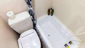 A bathroom with a toilet, a roll of toilet paper, a shower curtain, and a bathtub with a control panel. - Beach Resorts Hotel KALAKAUA (Onna)