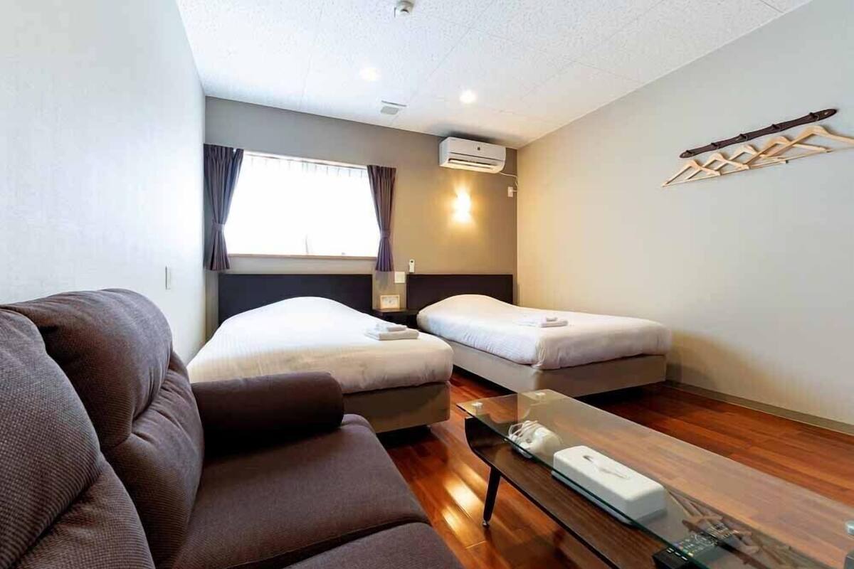 Habitación de hotel con sofá, dos camas, una mesa de centro de vidrio, un equipo de aire acondicionado y un tendedero de pared.