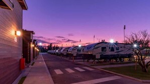 Une rangée de camping-cars est stationnée sur un parking, avec un bâtiment situé sur la gauche.
