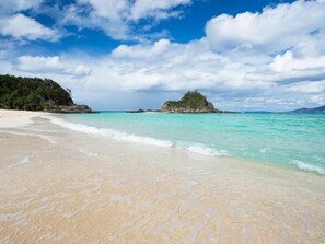 Una playa con aguas turquesas cristalinas, una orilla arenosa y una pequeña isla a lo lejos.