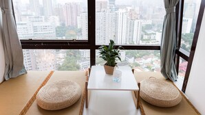 Une pièce avec vue sur le paysage urbain, une petite table sur laquelle est posée une plante en pot, et deux poufs en fibres tressées.