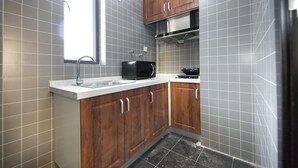 Une cuisine de taille réduite, avec des carreaux gris, des meubles en bois, un four à micro-ondes et un évier.