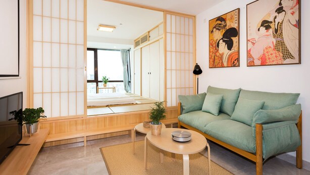 Un salon de style japonais traditionnel, avec un sol recouvert de tatamis, une basse table en bois, un canapé vert et des paravents coulissants de type shoji.