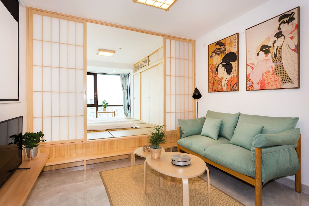 Ein traditioneller japanischer Wohnraum mit Tatami-Böden, einem niedrigen Holztisch, einem grünen Sofa und verschiebbaren Shoji-Schirmen.