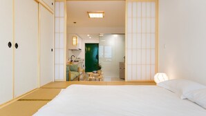Une chambre d’hôtel avec un sol recouvert de tatamis, un lit, un bureau avec une chaise et une porte verte.