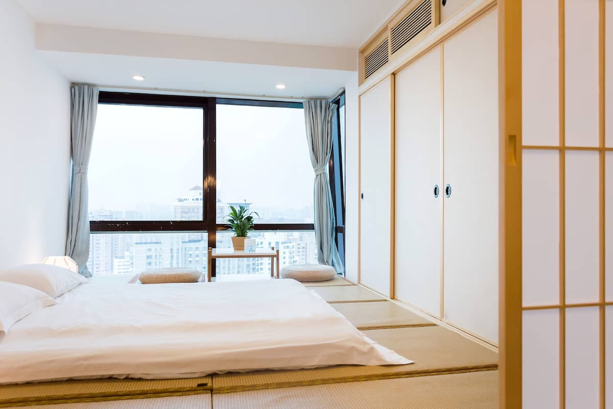 Ein Schlafzimmer mit einem großen Bett, Blick auf die Stadt, einem kleinen Tisch mit einer Pflanze und traditionellen Schiebetüren.