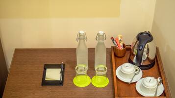 Una mesa de madera con un cuaderno, dos botellas de agua, un vaso, una cafetera y una bandeja con tazas y una cuchara.