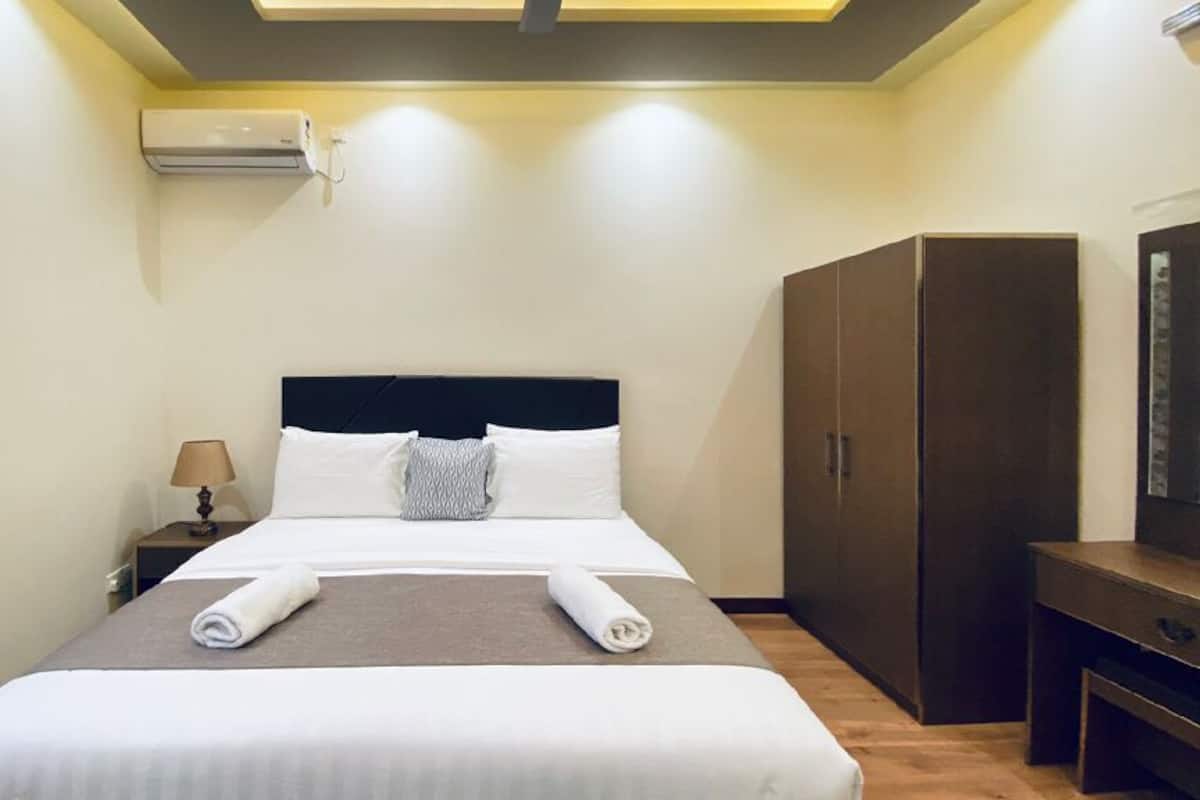 A hotel room with a bed, a wardrobe, a desk, and an air conditioning unit.