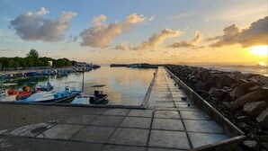 A marina with boats docked, a pier extending into calm waters, and a sunset in the background.