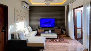 A modern living room with a flat-screen TV, a ceiling fan, and a chandelier.