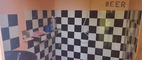 Un baño con pared de baldosas a cuadros blancos y negros, un lavabo, una pileta azul y un cartel que dice "SAVE WATER DRINK BEER".