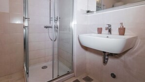 Un baño con cabina de ducha de vidrio, un lavabo blanco y un espejo sobre él.