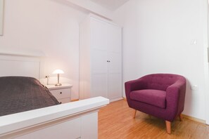 Makuuhuoneessa on sänky, yöpöytä, lamppu, vaatekaappi ja violetti nojatuoli.