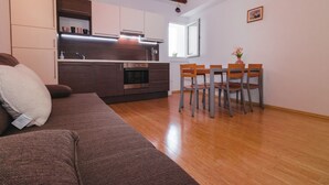 Cocina moderna con armarios oscuros, horno empotrado y zona de comedor con mesa de madera y cuatro sillas.
