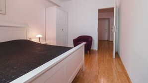 Un dormitorio con cama, una silla, un armario y una puerta que da a otra habitación.