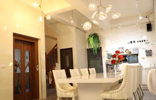 A modern dining area with a white table and chairs, a hanging plant, and a kitchen in the background. - Song Qian Brigade (Lukang)